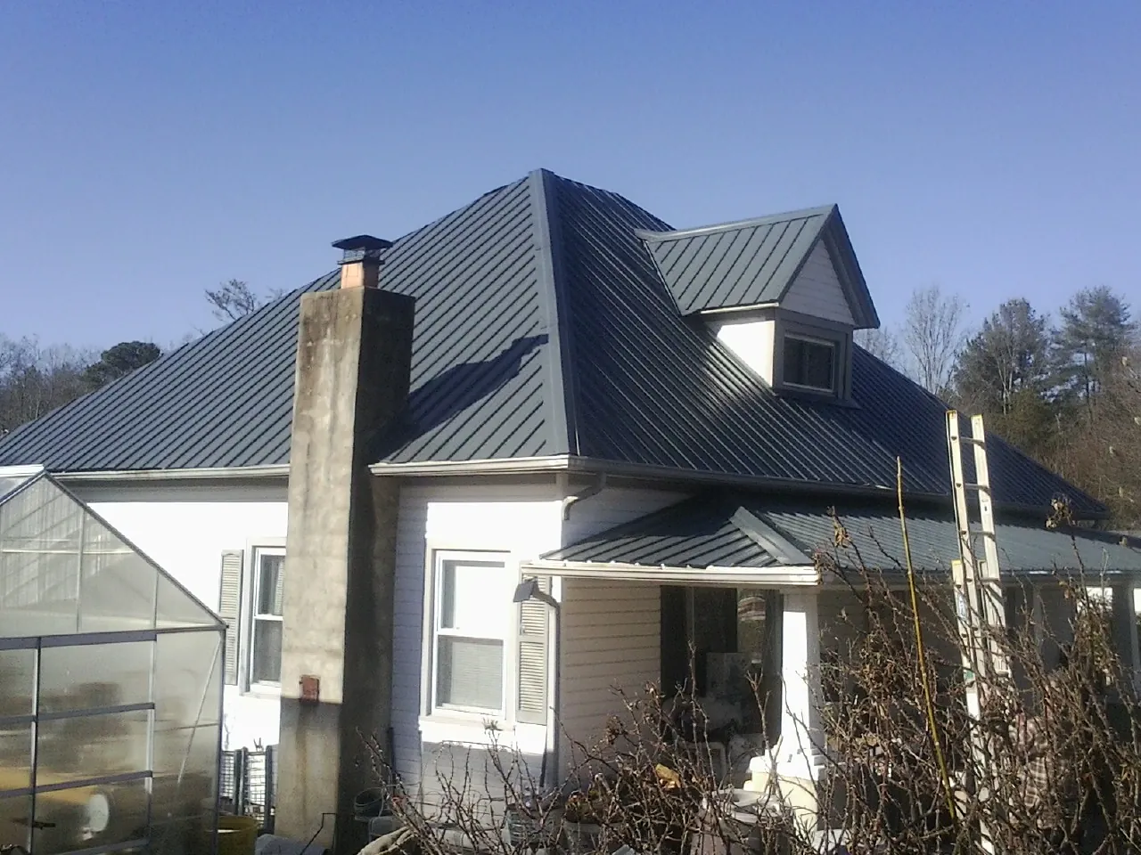 Dark blue standing seam metal roof on a white farmhouse with dormer — Slate & Tile Roof Repair by Roofing Brothers in New Richmond