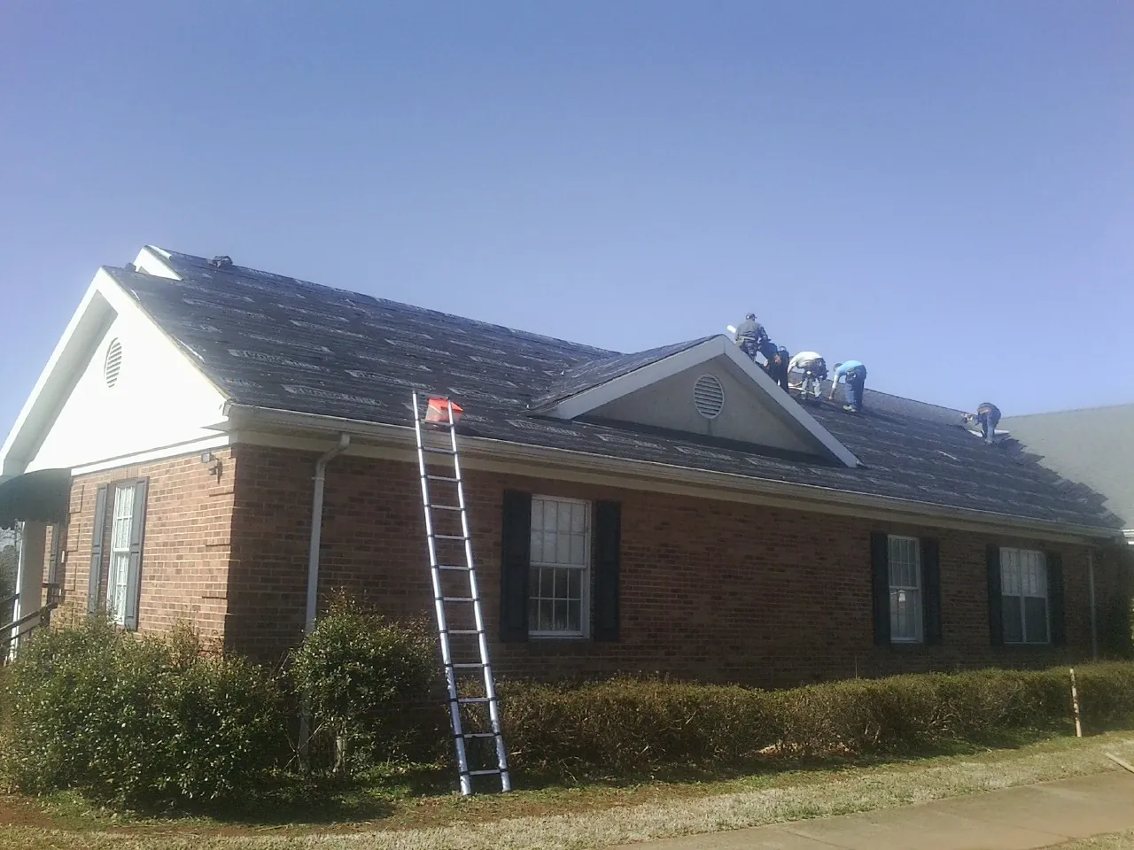 Crew tearing shingles off a brick ranch roof with a ladder set — Metal Roof Repair work by our crew in New Richmond