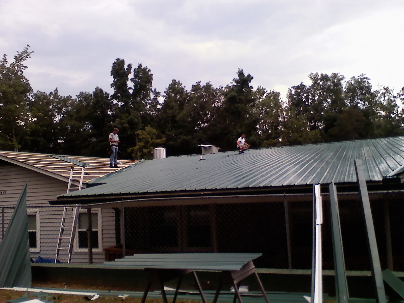 Two roofers installing green metal panels above a covered porch in New Richmond